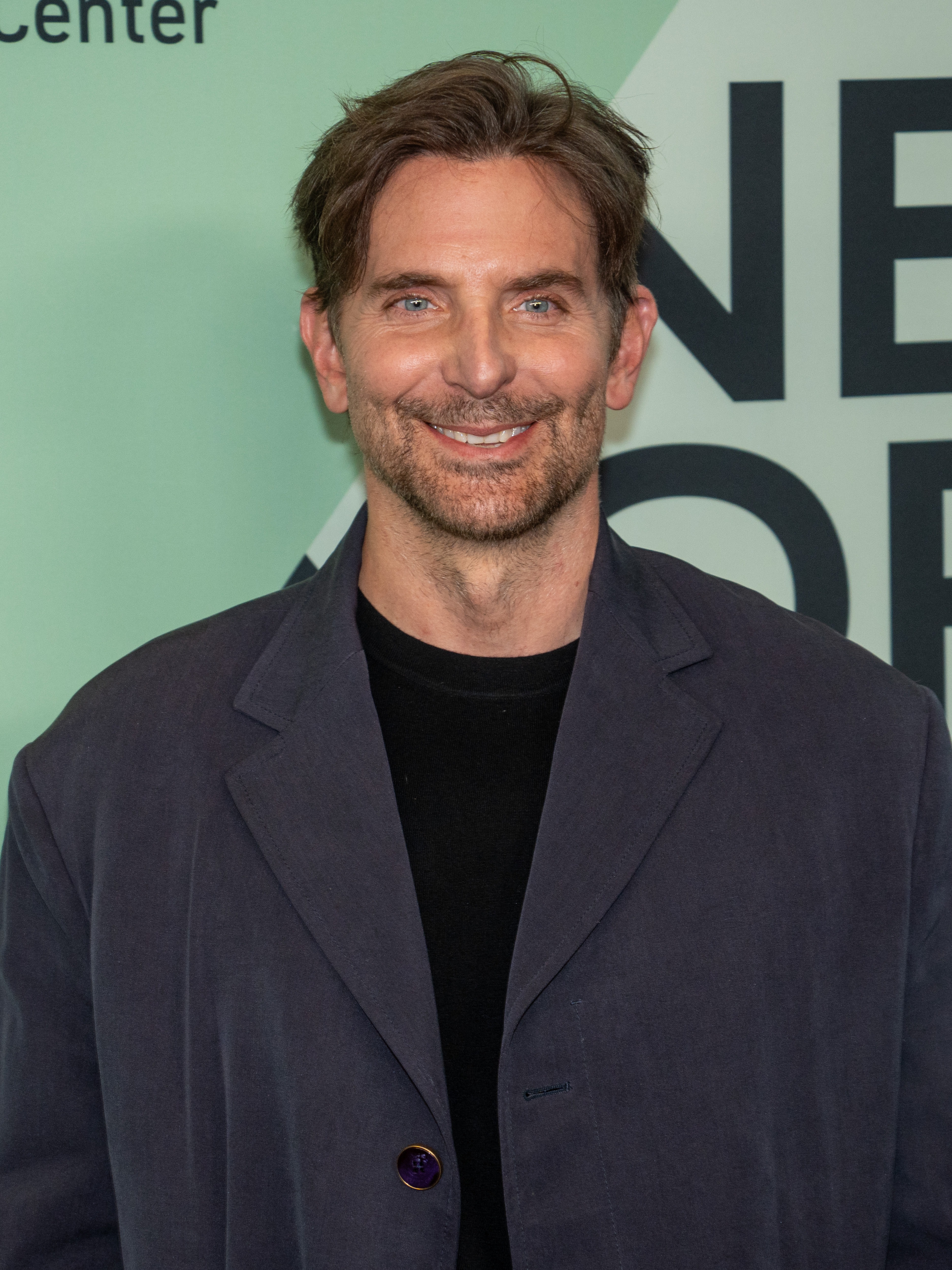 Bradley Cooper en una alfombra roja, sonriendo ante las cámaras